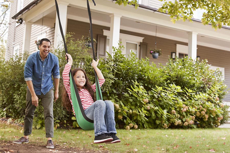 Blog - Dad Pushing His Daughter on a Green Fabric Tree Swing In Their Front Yard