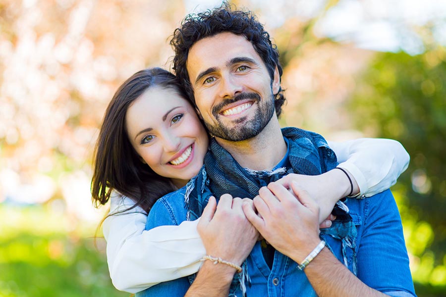 Personal Insurance - Young Couple Smiling, Wife Wrapping Her Arms Around Her Husband, Wearing Warm Blue and White Clothing