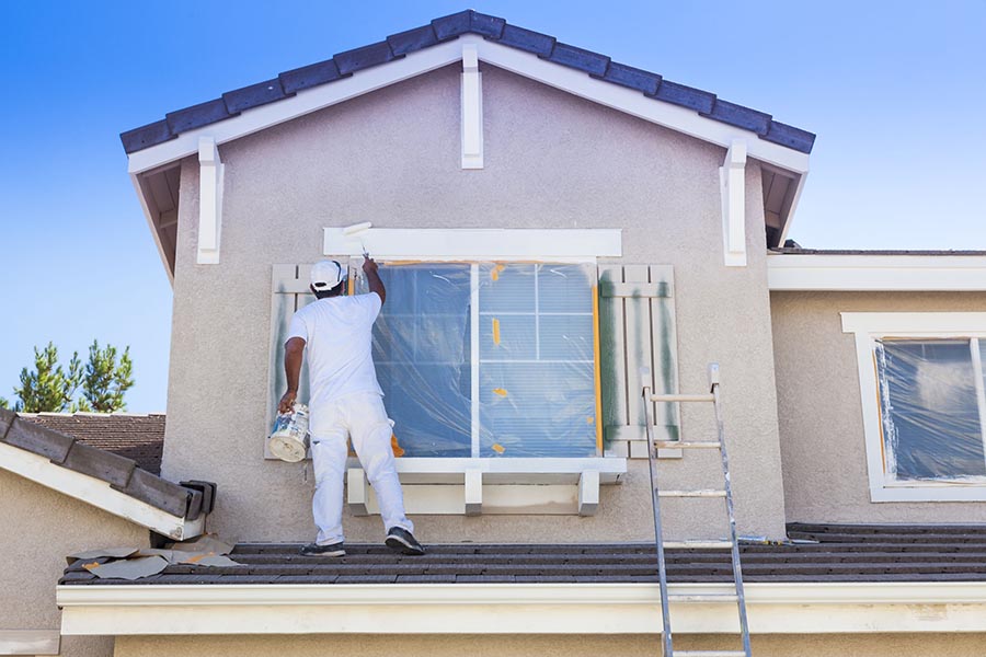 Specialized Business Insurance - Contractor Installing Windows and Painting Trim On a Stucco Home