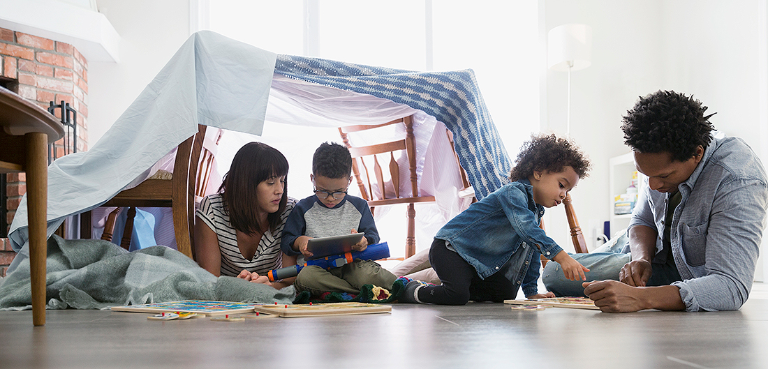 Mom, Dad, and two young children play on floor beneath blanket fort