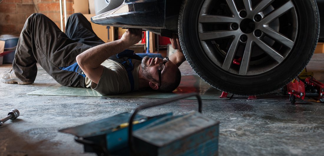 man lies down working on underside of car