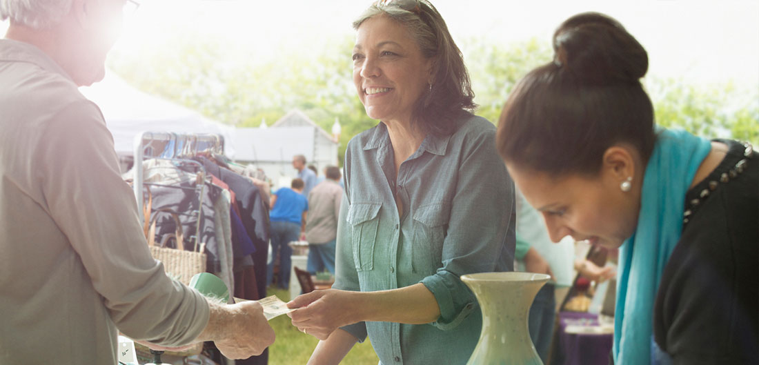 young woman purchases vase at garage sale while her friend looks on