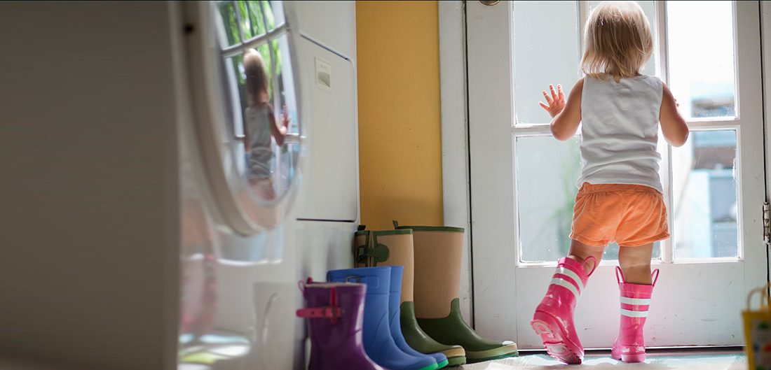 toddler in rain boots looks out back door of mudroom