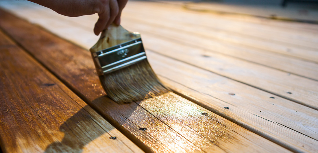 person using paintbrush to stain wooden deck