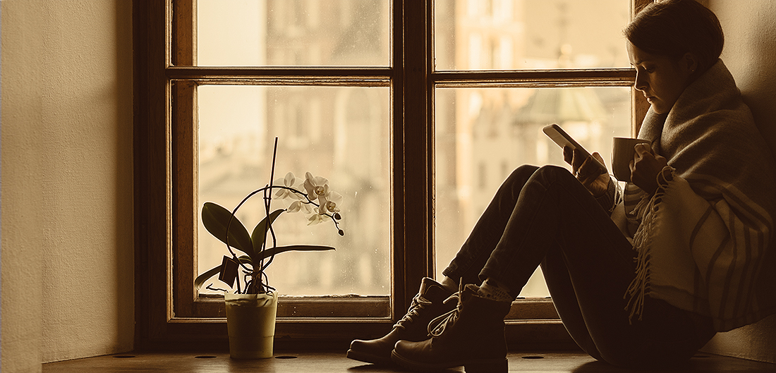 young woman reads book on chilly windowsill